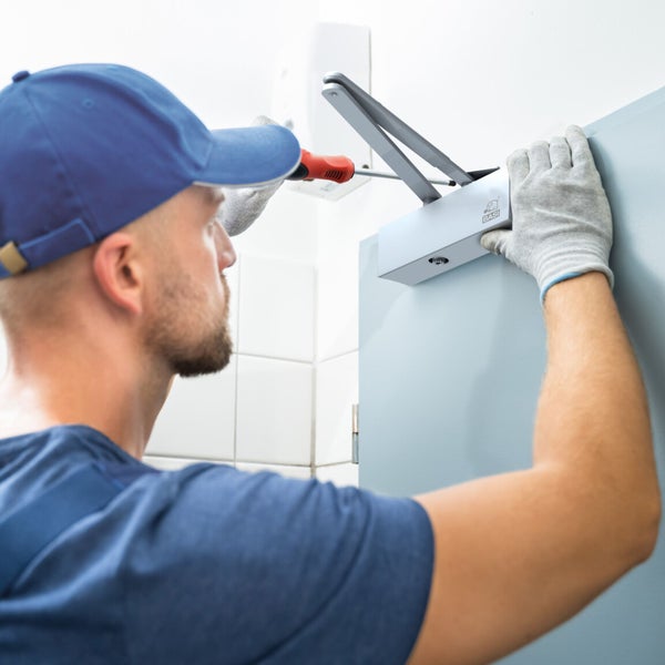 Monteur befestigt Türschließer mit Schraubendreher