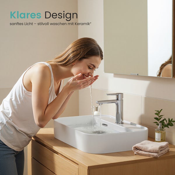 Frau wäscht sich Gesicht an einem Keramikwaschbecken mit Armatur auf einem Waschtisch im Badezimmer