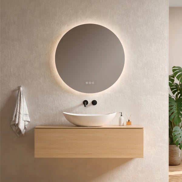 Modernes Badezimmer mit rundem, beleuchtetem Spiegel, weißem Aufsatzwaschbecken auf hellem Holz-Waschtischunterschrank und schwarzer Wandarmatur.