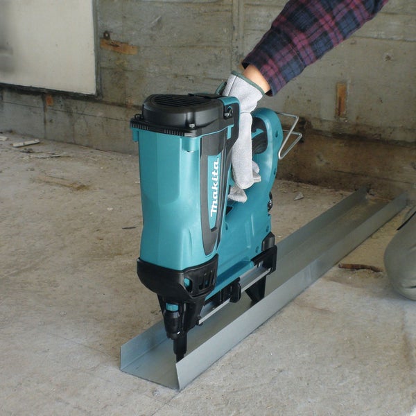 Ein Arbeiter verwendet einen Makita Bolzensetzgerät, um ein Metallprofil auf einem Betonboden zu befestigen.