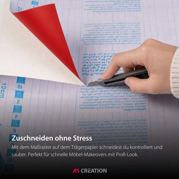 Hand schneidet mit einem Cuttermesser Klebefolie auf dem Maßraster des Trägerpapiers zu. AS Creation Logo.