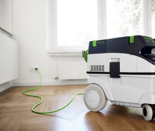 Festool Absaugmobil an einer Steckdose auf Holzboden in einem hellen Raum.