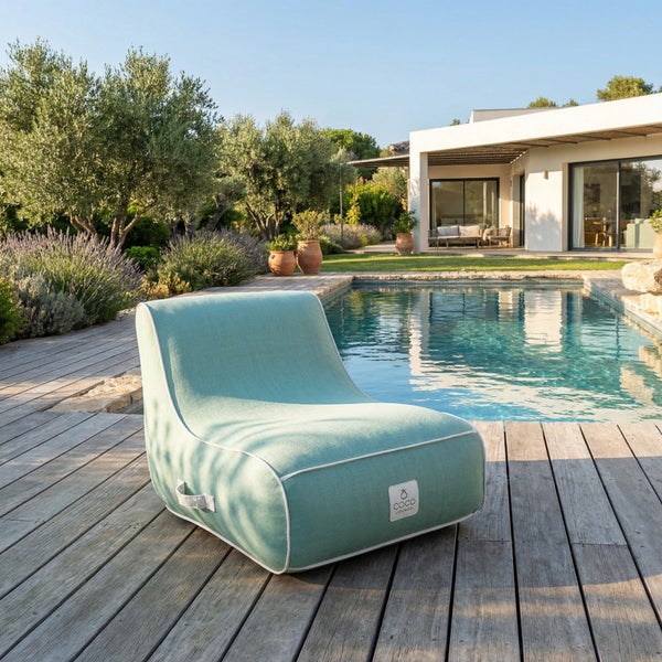 Moderner hellgrüner Loungesessel mit weißer Paspelierung auf einem Holzdeck am Pool, mit Schwimmbecken und Garten im Hintergrund.