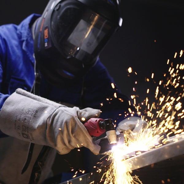 Person mit Schutzhelm und Schweißerhandschuhen beim Schweißen von Metall mit einem Schweißgerät, wodurch Funken entstehen