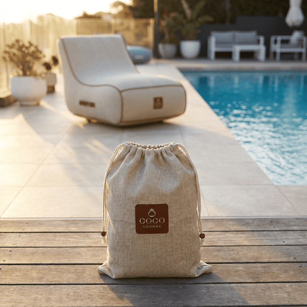 Textilbeutel mit Coco Lounge Logo auf einer Holzterrasse neben einem Pool und Loungemöbeln in einem hellen, modernen Außenbereich.