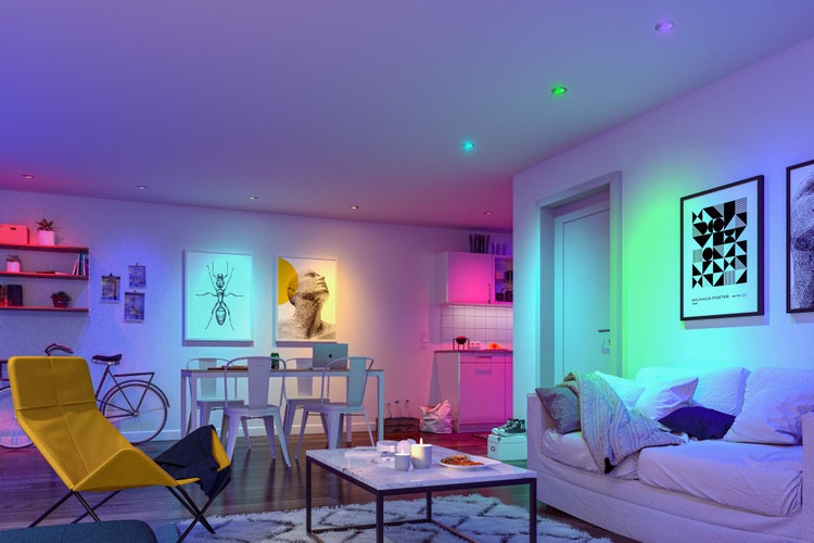 Wohnzimmer mit Sofa, Tisch, Stühlen, Beleuchtung und dekorativen Postern an der Wand, die eine helle und einladende Atmosphäre schaffen.