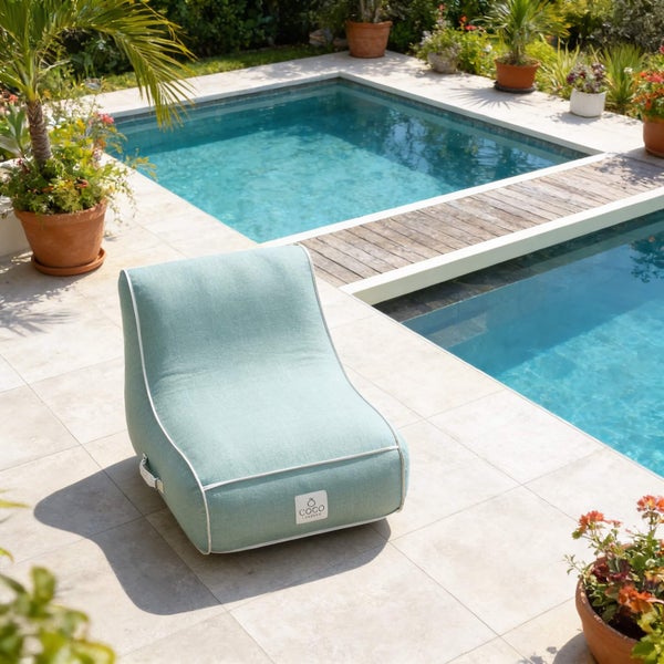 Moderner Outdoor-Sitzsack aus Stoff in Hellblau mit weißer Paspelierung auf einer hellen Fliesenterrasse an einem Pool.