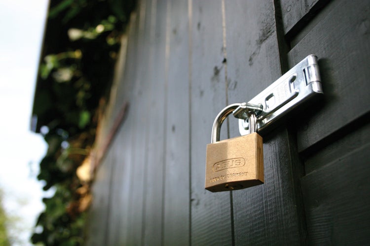 ABUS Vorhängeschloss aus Messing sichert eine Überfalle an einer dunklen Holztür.