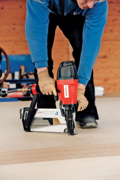 Eine Person bedient einen Druckluftnagler der Marke Haubold auf einem Holzboden.