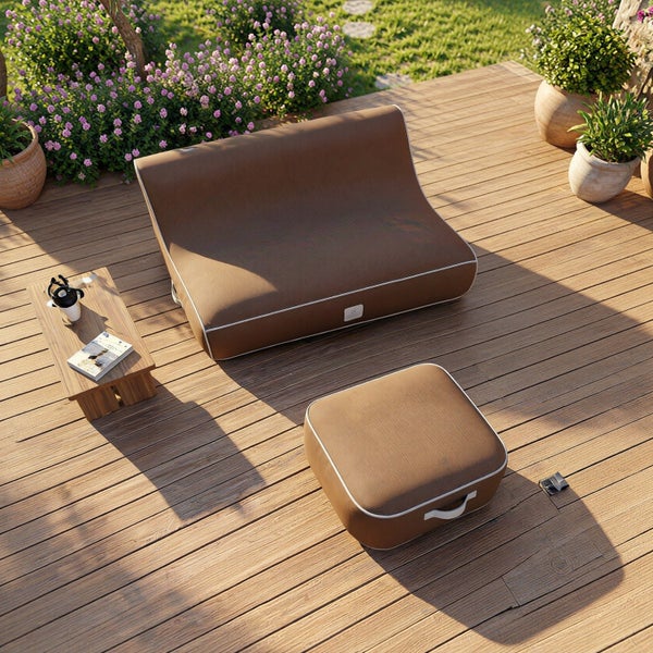 Moderne Outdoor-Lounge mit braunem Bodensofa und Hocker auf einer Holzterrasse in einem hellen Garten mit Pflanzen und Beistelltisch.