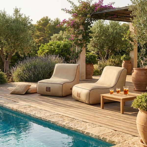 Zwei beige Outdoor-Sitzsäcke auf einer Holzterrasse neben einem Pool in einem Garten mit einem kleinen Beistelltisch aus Holz.