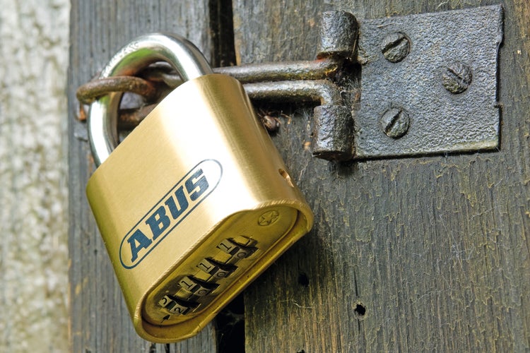 ABUS Zahlenschloss aus Messing mit ABUS Logo, befestigt an einem Metallriegel an einer verwitterten Holztür.