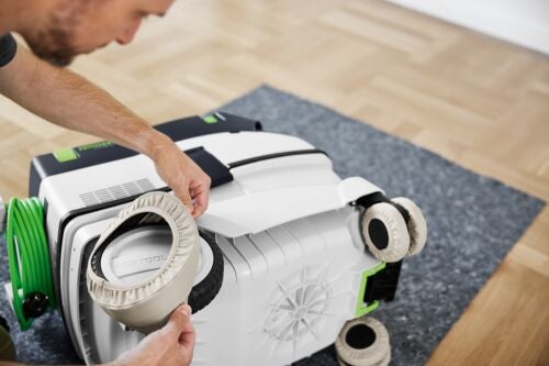 Eine Person zieht helle Stoff-Radschoner auf einen Festool Staubsauger zum Schutz von Parkettböden.