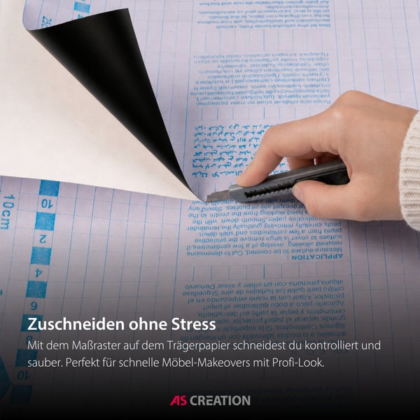 Eine Hand schneidet Klebefolie mit einem Cuttermesser entlang des Rasters auf dem Trägerpapier zu. AS Creation Logo.