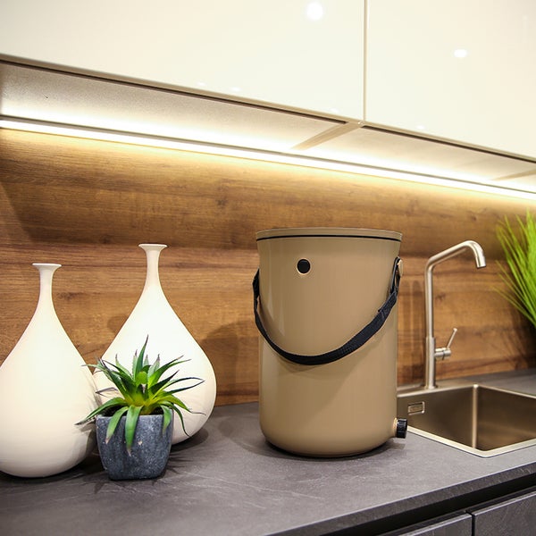 Küchenszene mit Komposteimer, Spüle und dekorativen Elementen auf einer Arbeitsplatte.