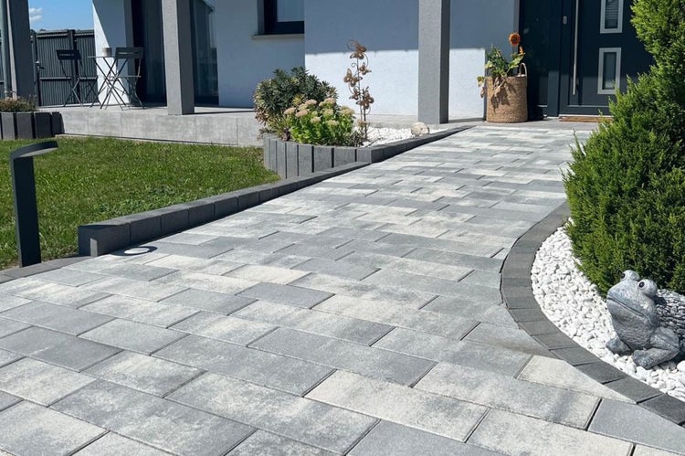 Moderner Gartenweg aus rechteckigen grauen Pflastersteinen, eingefasst mit Beton-Randsteinen, neben einer Rasenfläche und Zierkies.