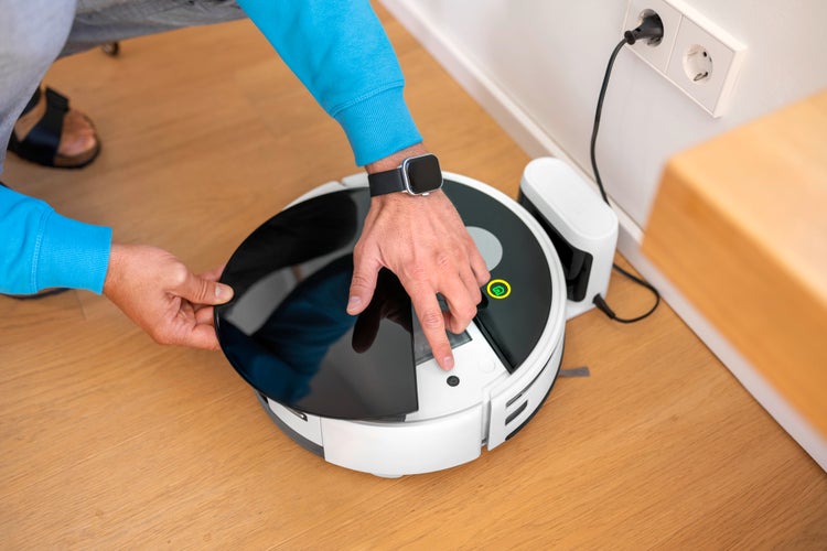Ein Mann bedient einen Saugroboter in einem hellen Raum.