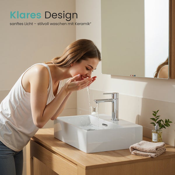 Frau wäscht sich das Gesicht an einem Aufsatzwaschbecken mit Armatur in einem hellen Badezimmer.