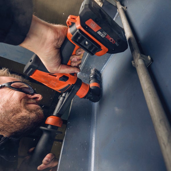 Handwerker mit Schutzbrille bohrt mit Fein Akku Bohrhammer in eine Metalloberfläche.