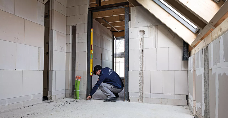 Rohbau eines Dachgeschosses mit Porenbetonsteinen und einem Handwerker, der eine Wasserwaage benutzt
