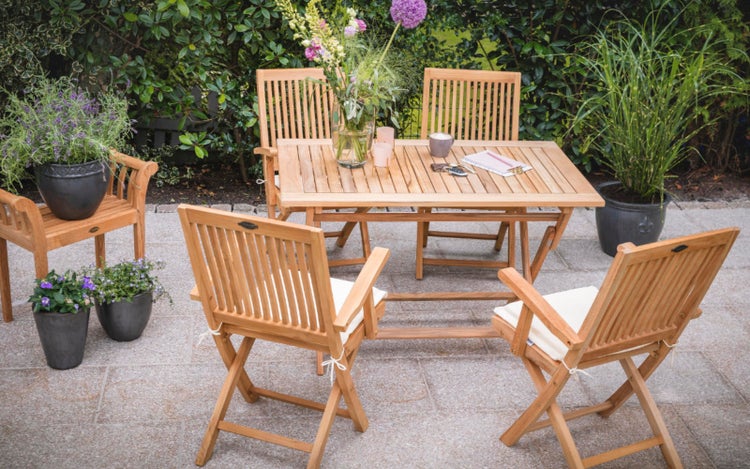 Gartenszene mit Holztisch und Holzstühlen, Blumen und Pflanzen in Töpfen