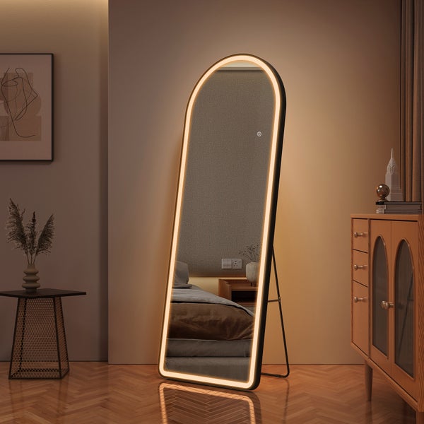 Bodenstehender Standspiegel mit bogenförmigem Design, schwarzem Rahmen und umlaufender LED-Beleuchtung in einem wohnlichen Zimmer.