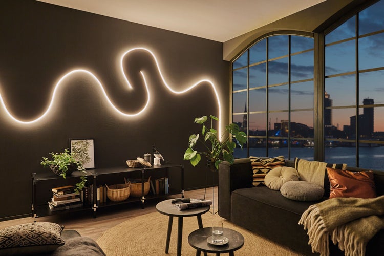 Wohnzimmer mit schwarzer Wand, linearem Licht an der Wand, Regal, Sofa und großem Fenster mit Blick auf die Stadt