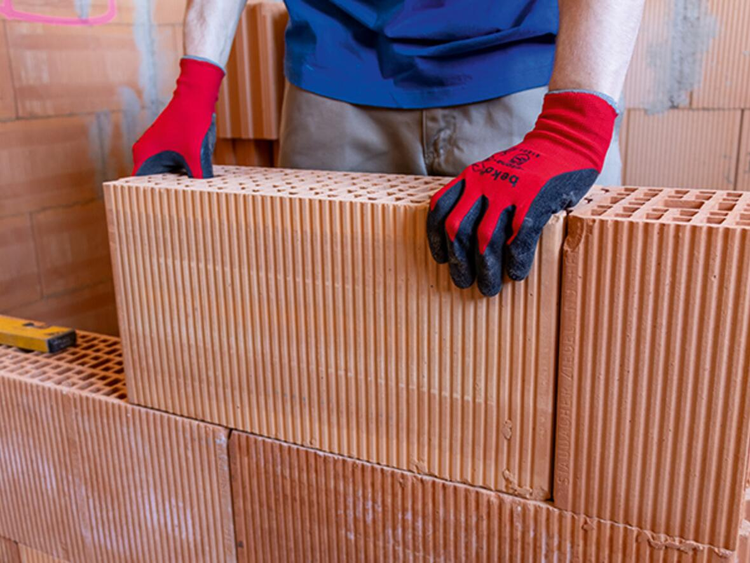 Mann mauert Ziegelwand mit Lochziegel und Arbeitshandschuhen
