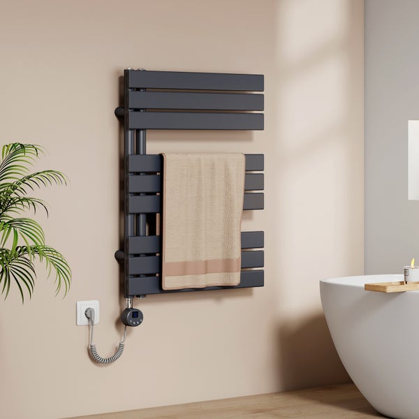 Moderner elektrischer Handtuchheizkörper in Anthrazit mit digitalem Thermostat in einem hellen Badezimmer neben einer Badewanne.