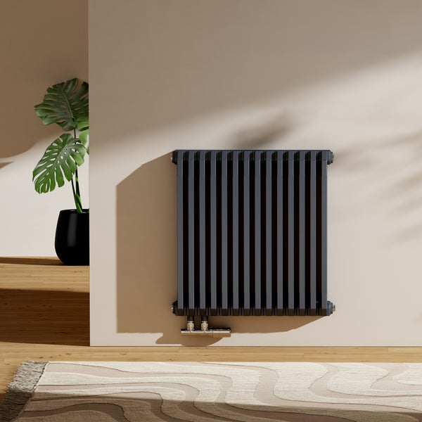 Grauer Heizkörper an einer Wand mit Teppich und Topfpflanze