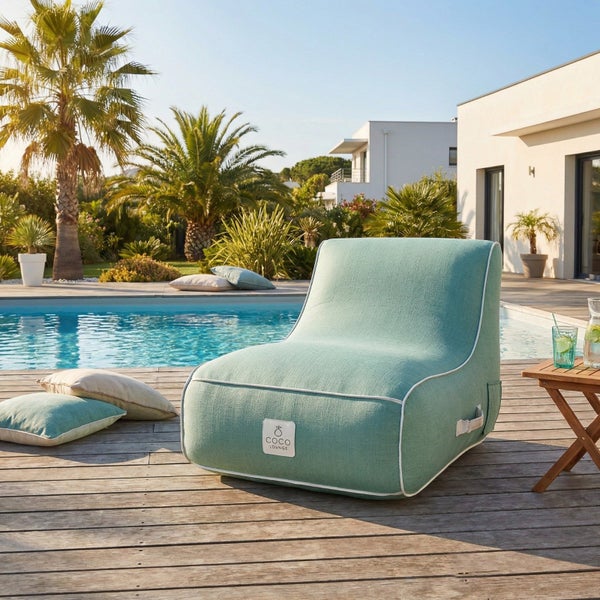 Moderner Outdoor-Sitzsack mit Coco Lounge Logo auf Holzterrasse am Pool. Helle, geräumige Atmosphäre mit Palmen und modernem Haus.