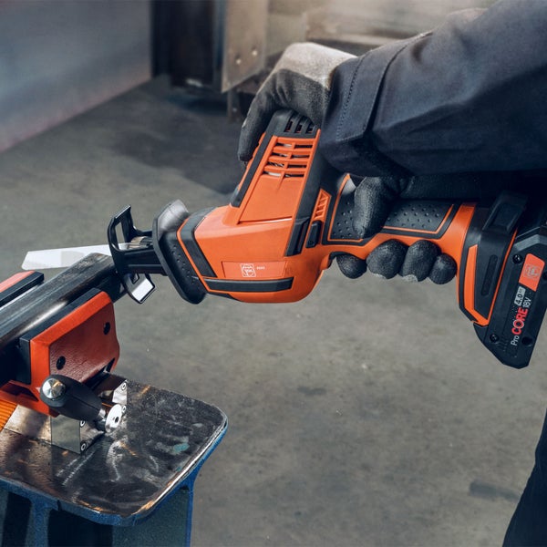 Person mit Handschuhen verwendet eine Fein Akku-Säbelsäge zum Schneiden eines Metallrohrs, das in einem Schraubstock eingespannt ist.