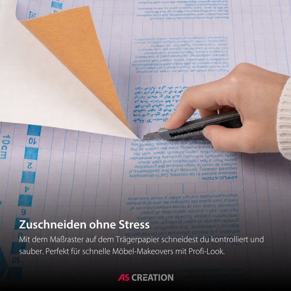Eine Hand schneidet mit einem Cuttermesser eine strukturierte Klebefolie auf dem Trägerpapier mit einem Maßraster zu. AS Creation Logo.