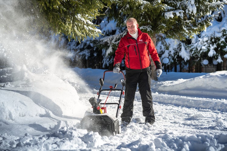 Ein Mann bedient eine Solo by AL-KO Schneefräse, um Schnee bei sonnigem Winterwetter von einem Weg zu räumen.