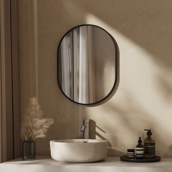 Badezimmer mit ovalem Wandspiegel, Aufsatzwaschbecken aus Steinoptik, moderner Armatur und dekorativen Accessoires in natürlichem Ambiente.