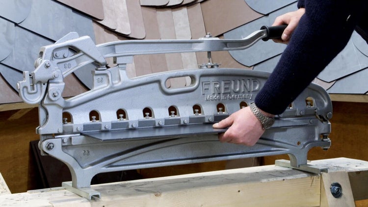 Person bedient eine FREUND Schieferschere zum Zuschneiden von Schieferplatten auf einer Holzunterlage.