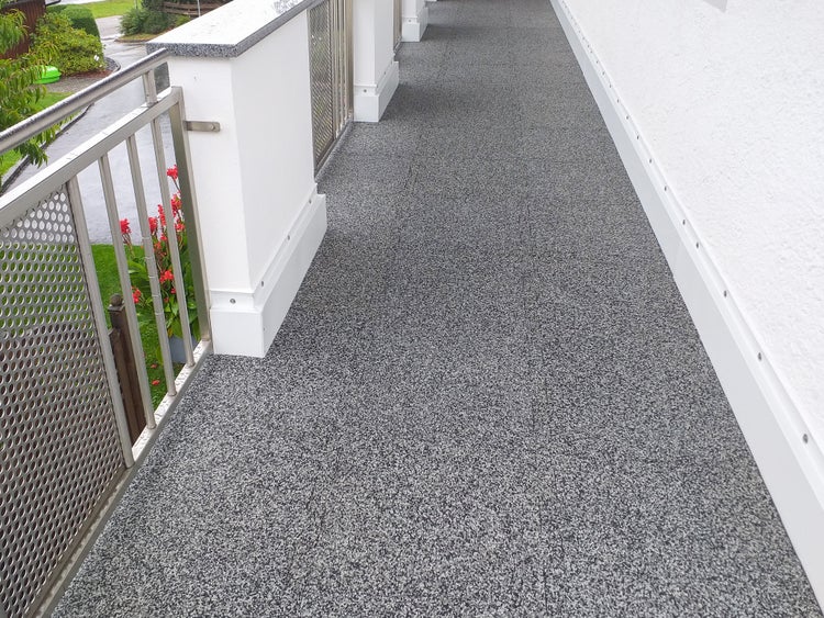 Moderner Balkon mit grauem Steinteppich-Bodenbelag und Edelstahlgeländer.