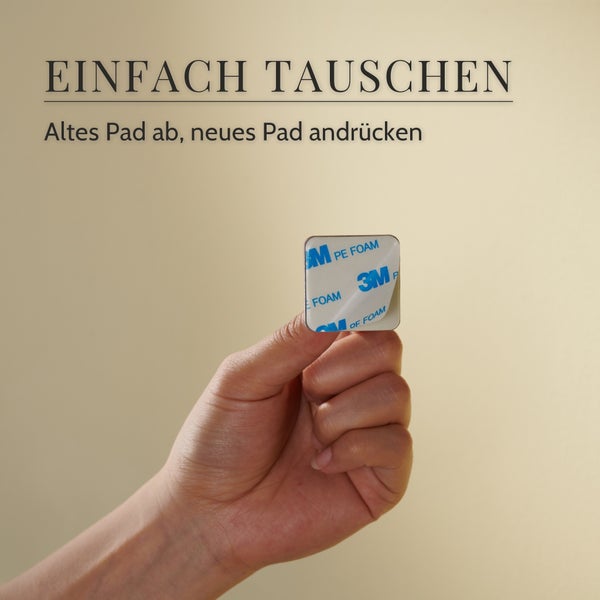 Hand hält ein quadratisches Klebepad mit abziehbarer Schutzfolie zum Austausch von Halterungen