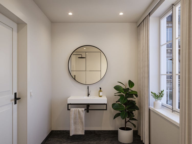 Modernes Badezimmer mit weißem Wandwaschbecken, schwarzer Armatur, rundem Spiegel und einer großen Zimmerpflanze.