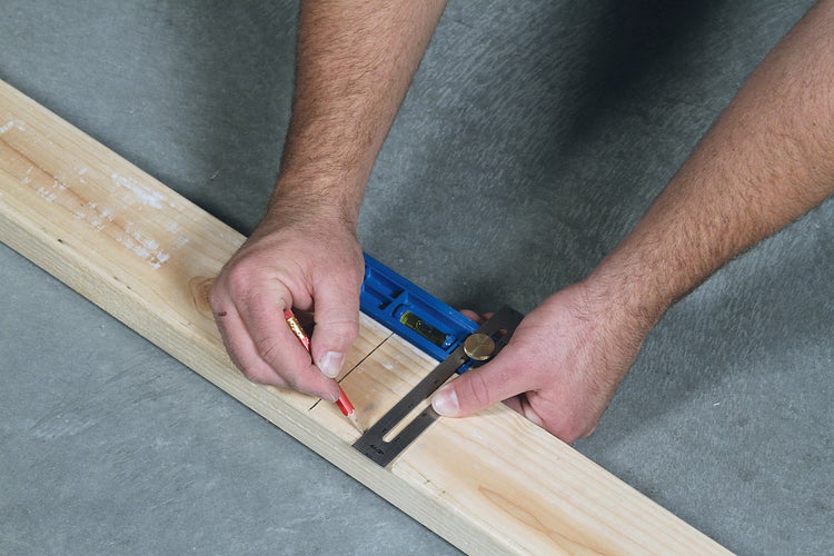 Eine Person markiert ein Holzbrett mit einem Winkel und einem Bleistift.