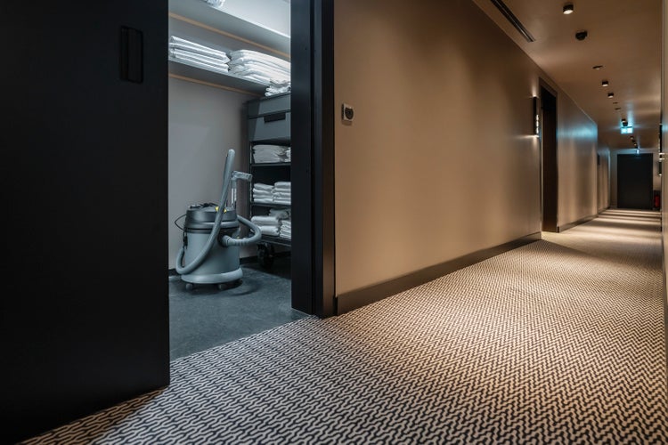 Nass-Trockensauger in einem Lagerraum neben einem Hotelflur mit gemustertem Teppich.