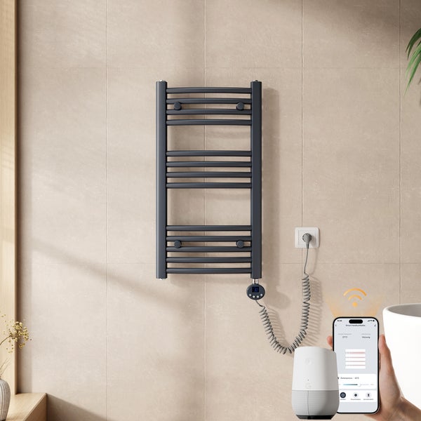 Elektrischer Badheizkörper an gefliester Wand mit digitaler Anzeige und Spiralkabel, steuerbar über Smartphone-App und Smart-Speaker.