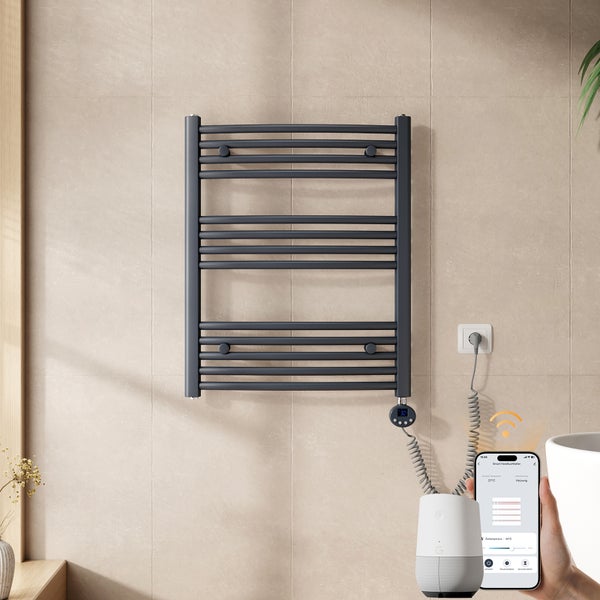 Moderner elektrischer Handtuchheizkörper in Dunkelgrau an einer gefliesten Wand, steuerbar per Smartphone-App und Smart Speaker.