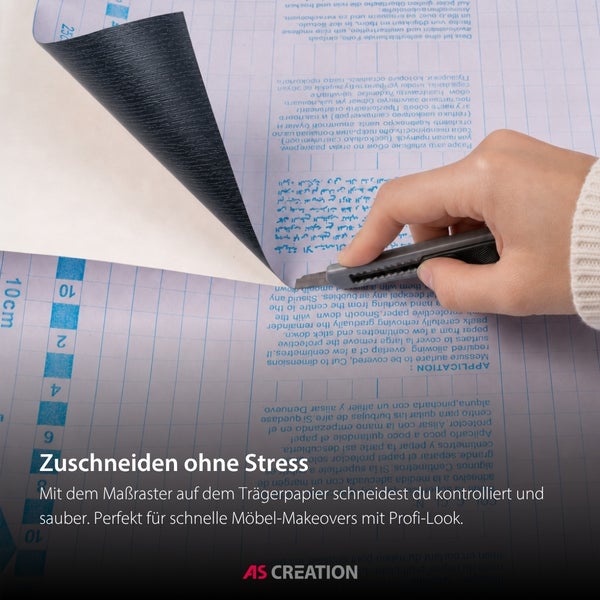 Hand schneidet selbstklebende Folie mit einem Cuttermesser entlang des Maßrasters auf dem Trägerpapier.