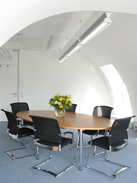 Konferenzraum mit ovalem Tisch, Bürostühlen und Blumenarrangement