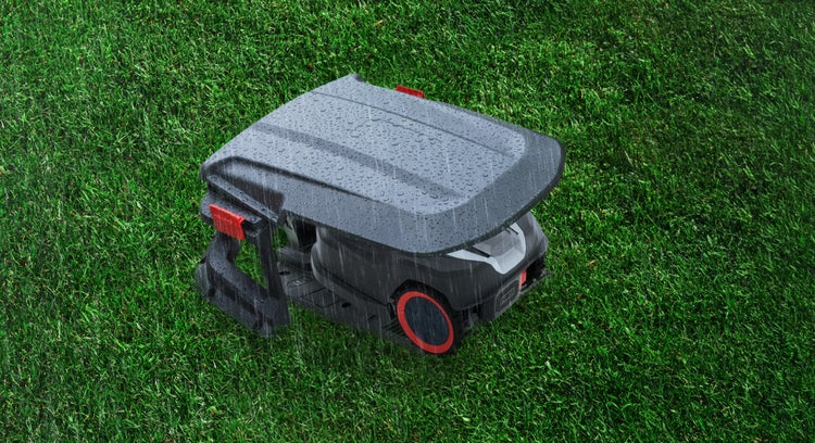 Wetterfeste Mähroboter-Garage aus Kunststoff auf einer Rasenfläche im Regen mit einem untergestellten Mähroboter.