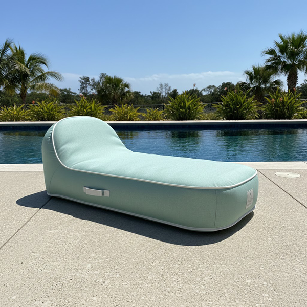Ergonomische Outdoor-Poolliege an einem Swimmingpool, hellgrüner Stoff mit weißer Paspelierung und seitlichem Tragegriff.