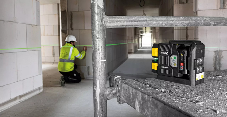 Stabila Logo. Ein Bauarbeiter verwendet einen Kreuzlinienlaser von Stabila auf einer Baustelle, um horizontale Linien an den Wänden zu markieren.