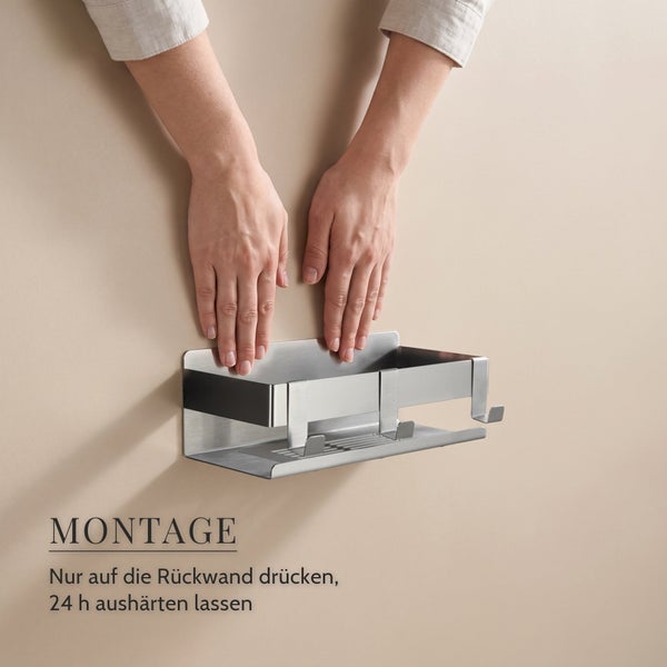 Hände drücken eine metallene Duschablage mit Haken gegen eine Wand zur Montageanleitung für eine klebbare Badablage.