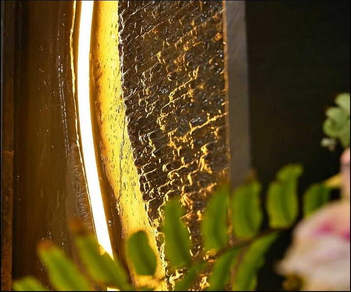 Nahaufnahme eines beleuchteten Wasserfalls mit Pflanzendetails im Vordergrund.